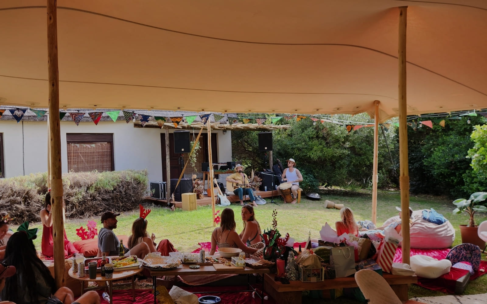 Friends gathered under a canvas tent decorated with bunting during a daytime backyard party