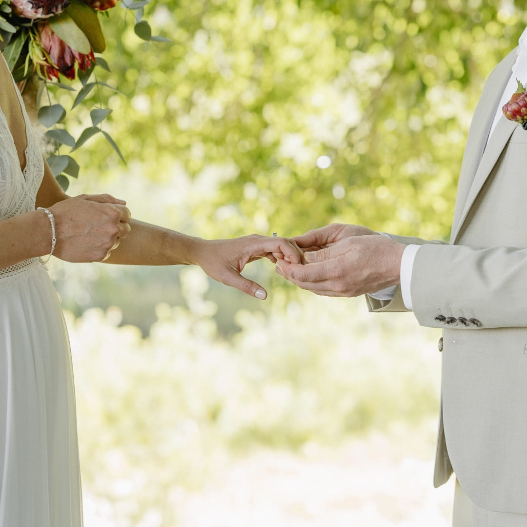 A bride and groom hold hands outdoors surrounded by greenery