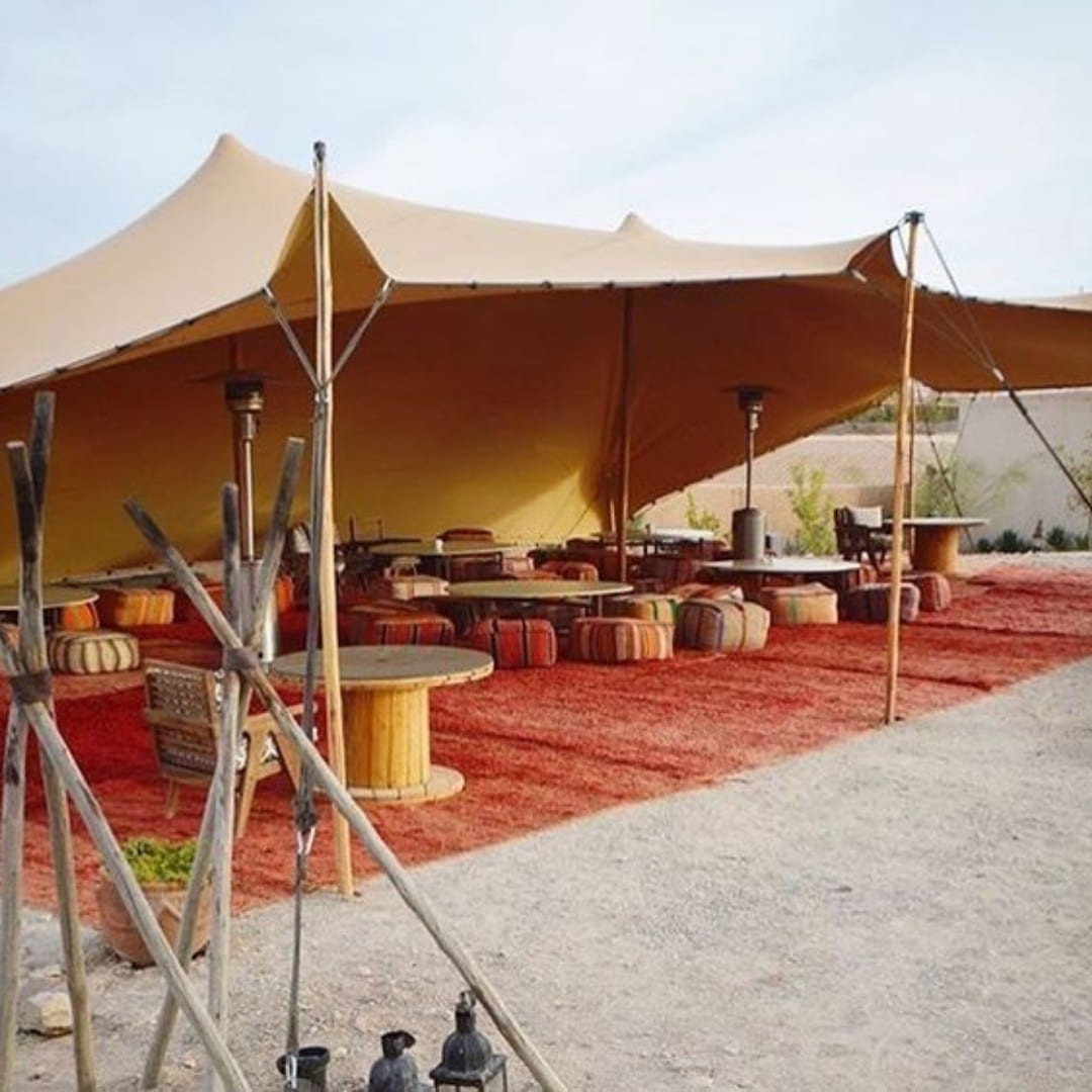 A canvas tent set up as a lounge area with a red rug, low tables and floor cushions