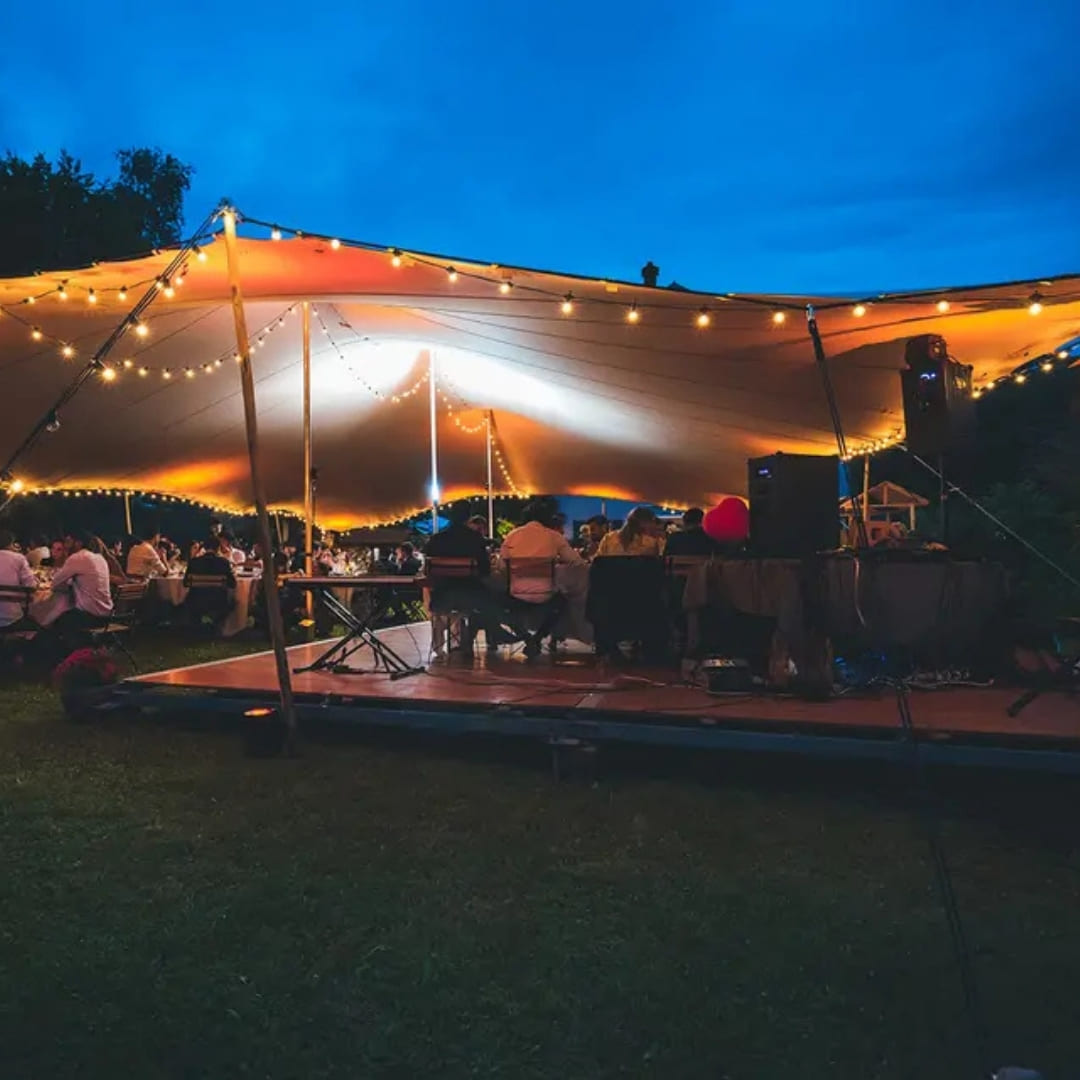 A canvas tent with a lit dance floor and live band performing at dusk