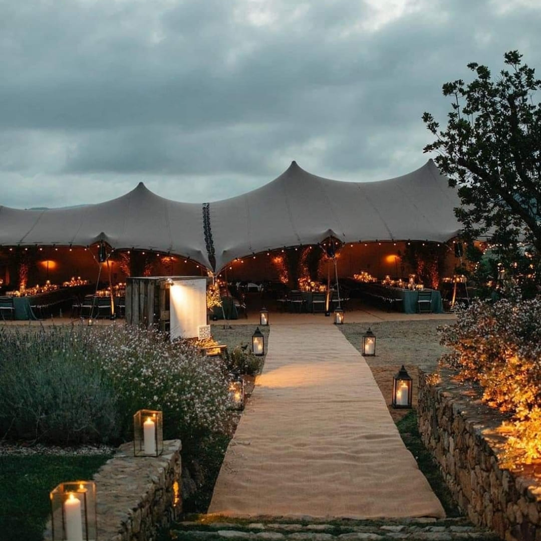 A canvas tent glowing at twilight beside a candlelit pathway lined with lanterns