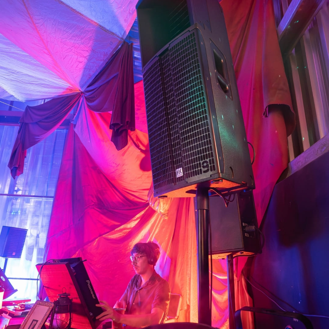 A DJ on CDJ's inside a canvas tent lit with pink and blue lighting