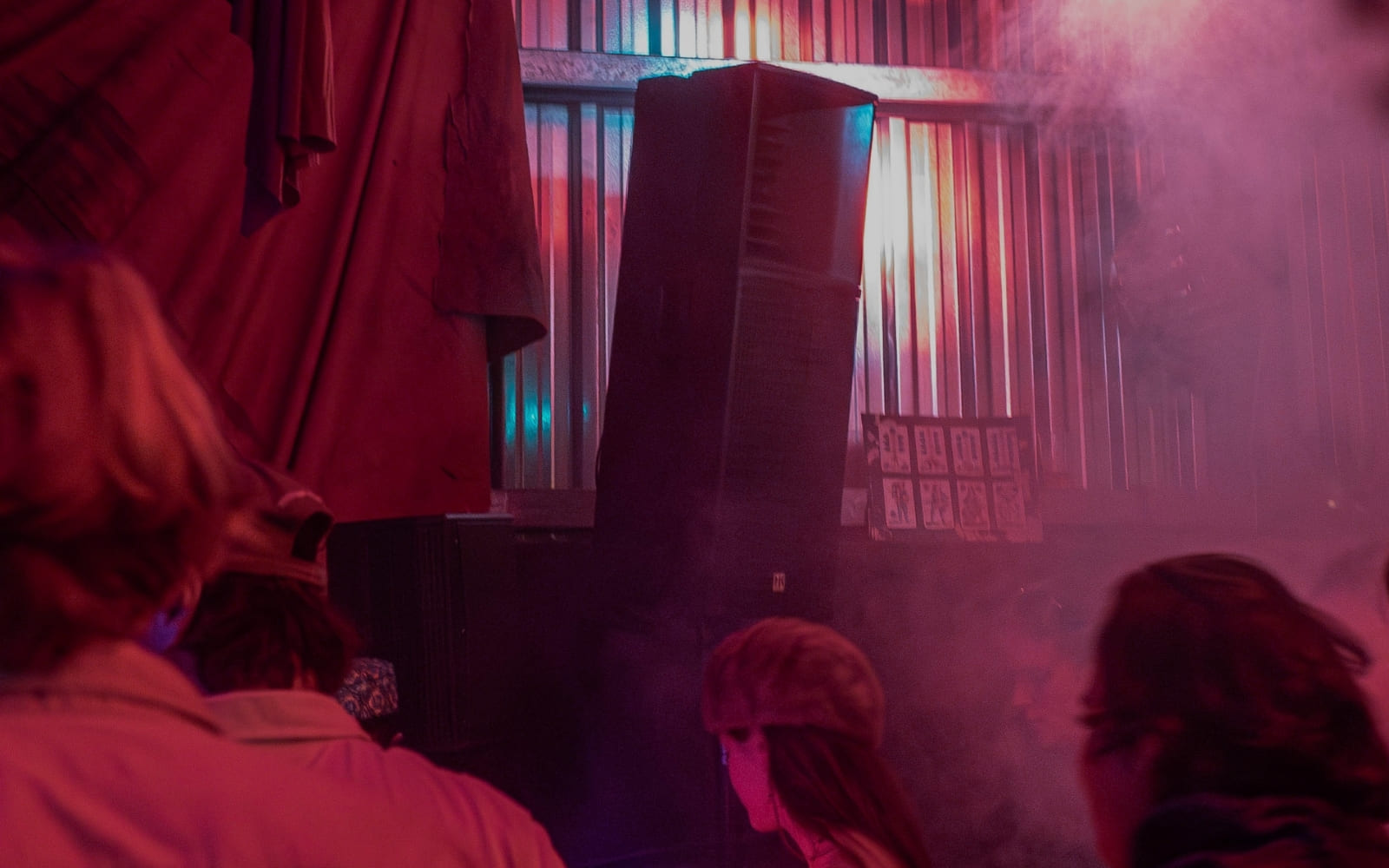 A large speaker glows red and pink under smoke and lighting at an indoor event