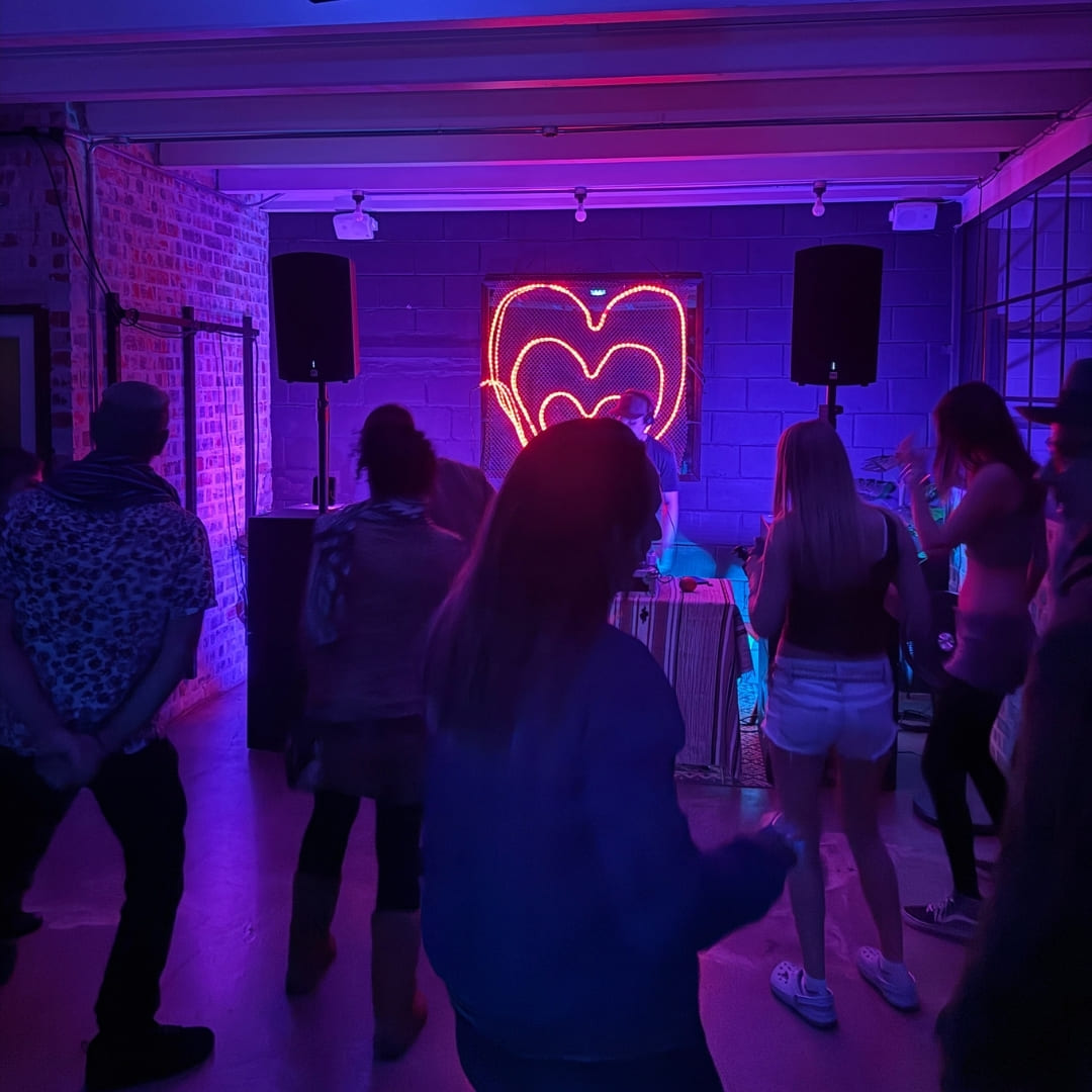 Guests dance indoors under blue and purple lighting near a neon heart sign