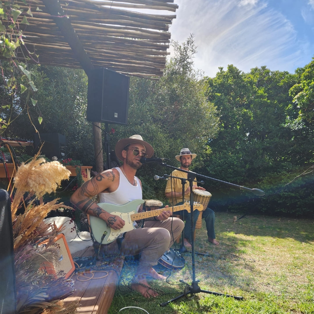 Two musicians performing acoustic guitar and percussion in a garden setting