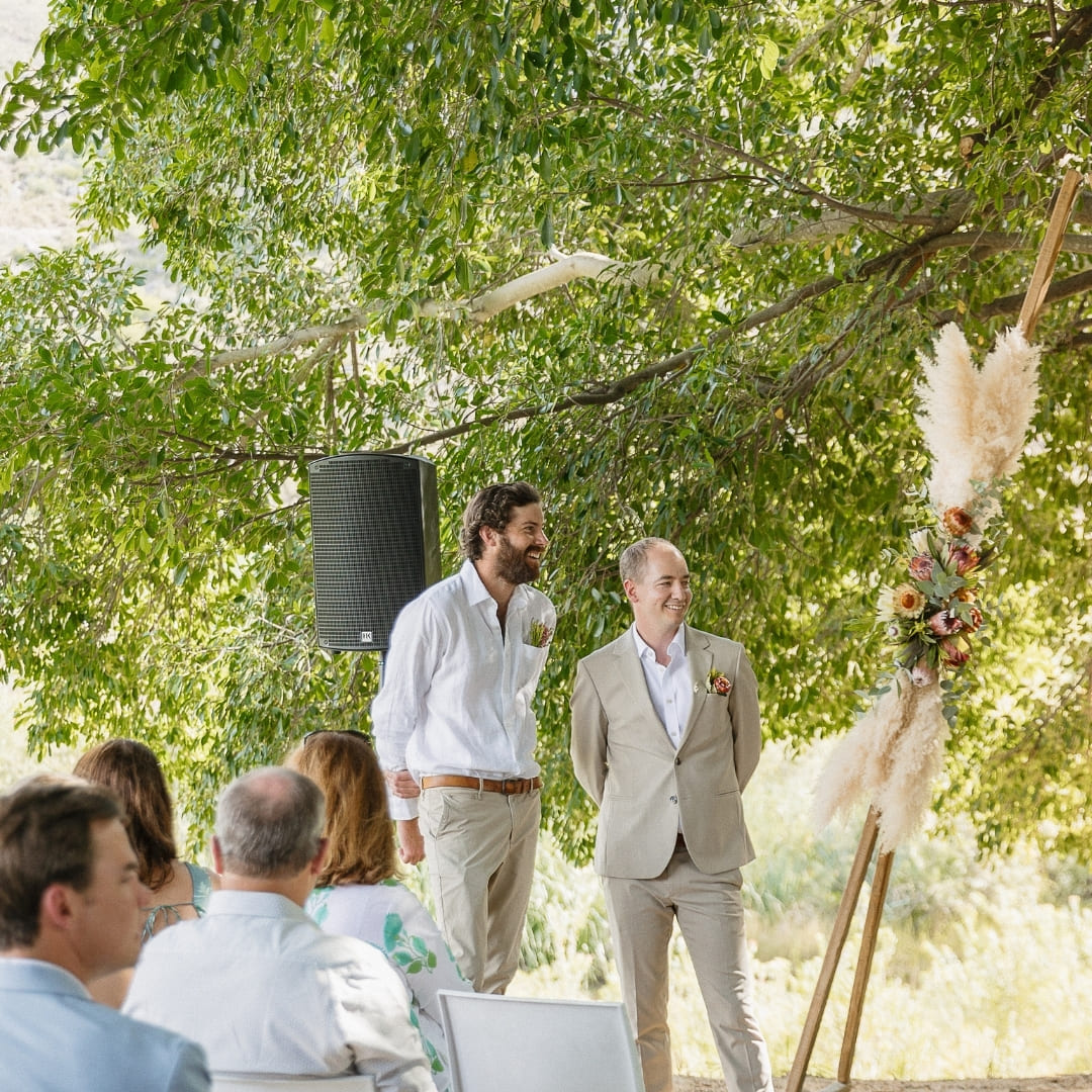 A groom stands beneath a large banyan tree during their outdoor wedding ceremony