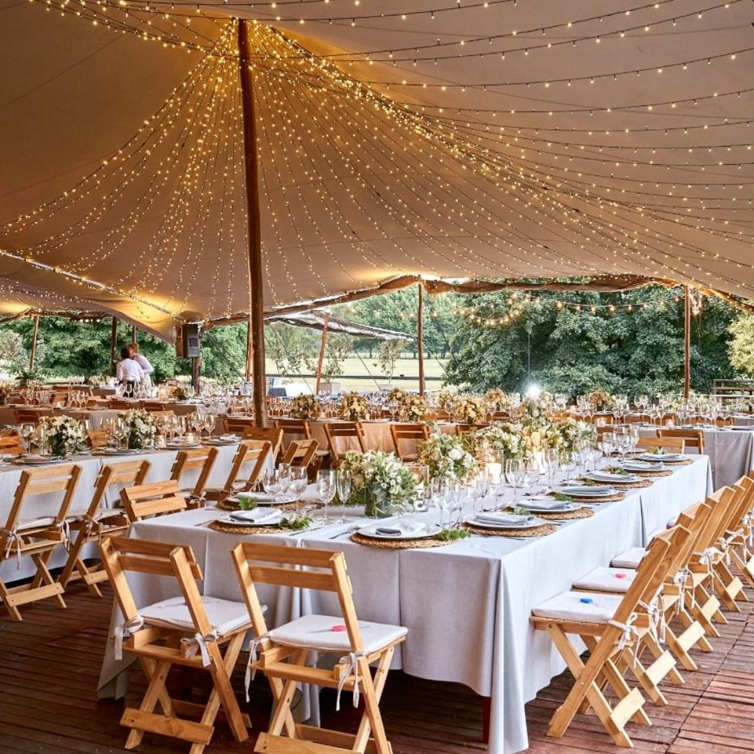 A canopy of string lights hangs above a long table set for a wedding reception