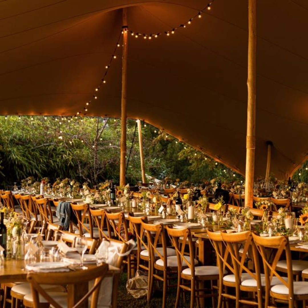Long dining tables set for a wedding reception under a canvas tent strung with lights