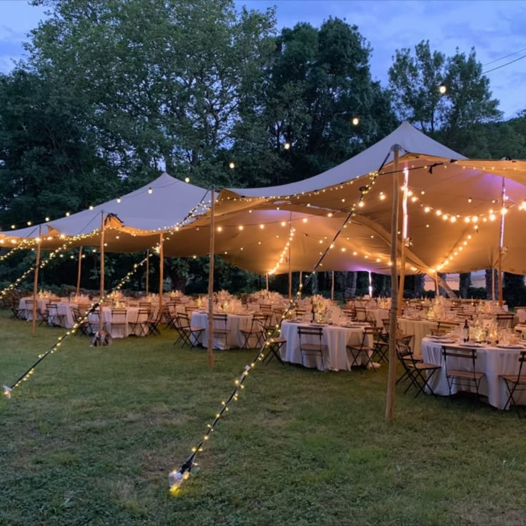 A canvas tent lit with string lights over long tables set for a wedding reception at dusk