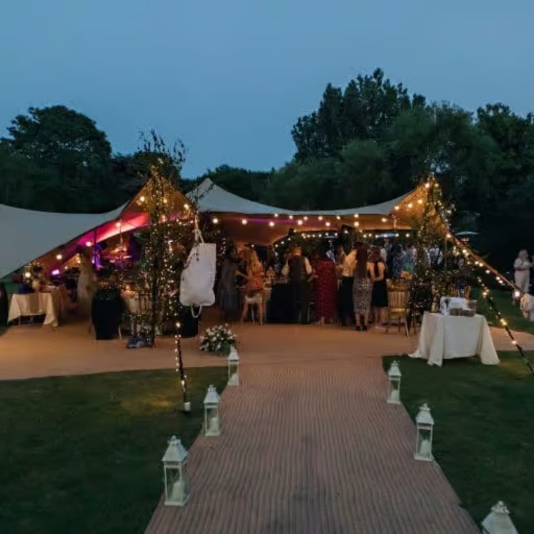 Guests gather under a canvas tent decorated with string lights during a wedding reception at dusk