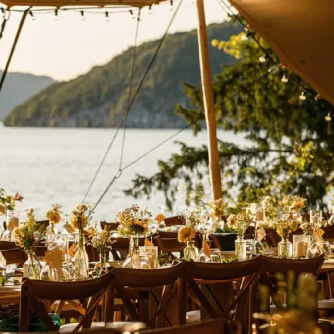 A canvas tent set up beside water with tables decorated with sunflowers